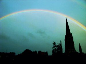 A rainbow over a church with a steeple in the background.