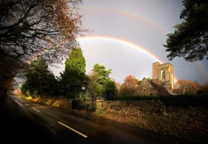 A rainbow is seen over a road and church.