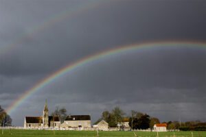 A rainbow over a church in a field.