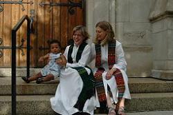 Two women in white robes sit on the steps of a church.