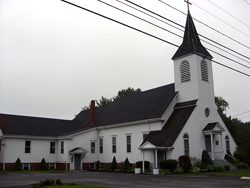 A white church with a steeple in the middle of the road.