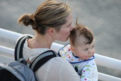 A woman with a baby in a backpack kisses her baby.