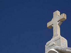 A cross on top of a white building against a blue sky.