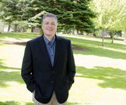 A man in a blazer standing in a grassy area.