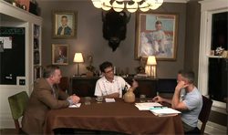 Three men sitting around a table in a living room.