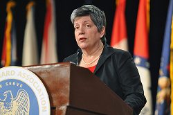 A woman standing at a podium in front of flags.