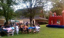 A group of people sitting at tables in a yard with a bouncy castle.