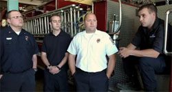 Four firefighters standing in front of a fire truck.