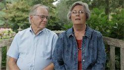 An older couple sitting on a wooden bench.