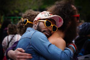 A man with a hat and sunglasses is hugging another man.