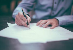 A person signing a document with a pen.