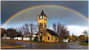 A church with a clock tower under a rainbow.