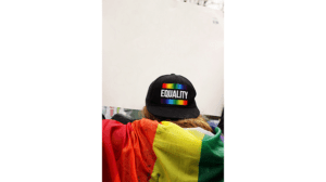 A person wearing a black hat with a rainbow flag on it.