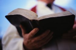 A priest holding a bible in front of a blue sky.