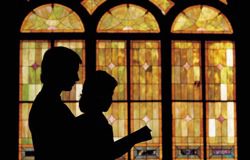 A silhouette of a man and a child in front of a stained glass window.