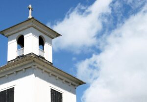 A white church with a steeple against a blue sky.