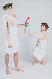 Two men dressed in greco-roman garb holding a rose.