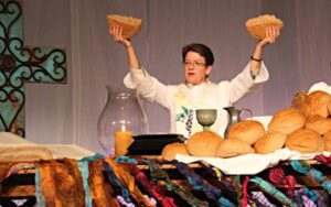 A woman is holding up a bunch of bread in front of a table.