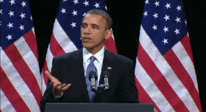 President barack obama speaks at a podium in front of american flags.