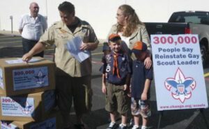 A boy scout stands next to a box of boxes.