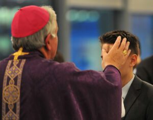 A priest is putting a rosary on a man's head.