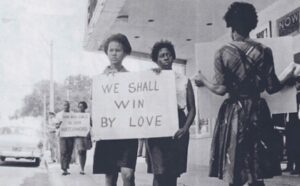 Two women holding signs that say we shall win by love.