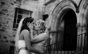 Two brides kissing in front of a church.