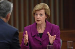 A woman in a purple suit is talking to a man at a table.