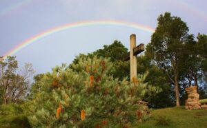 A rainbow over a cross on a hill.