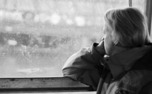 A black and white photo of a woman looking out a window.