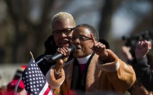 A woman is holding an american flag and speaking into a microphone.