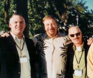 Four men posing for a picture in front of a palm tree.