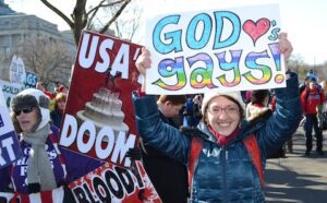 A woman holds up a sign that says god is gay.