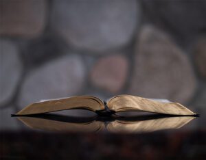 An open bible on a table in front of a stone wall.