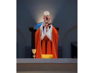 A priest in an orange robe holds up a white plate.