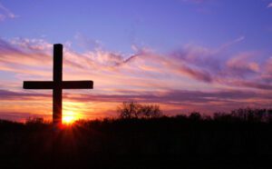 A cross is in the middle of a field with a sunset behind it.