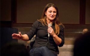 A woman in a black shirt is speaking into a microphone.