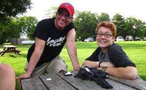 Two people smiling at a picnic table in a park.