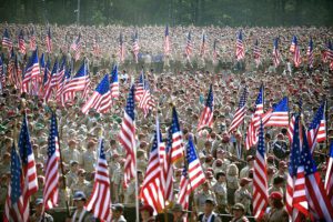 A large group of people holding american flags in a field.