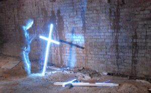 A man with a cross in front of a brick wall.