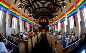 The inside of a church with rainbow flags hanging from the ceiling.