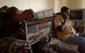 Two men sitting on a couch reading a newspaper.