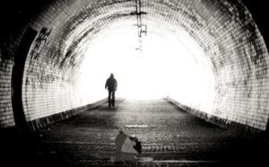 A black and white photo of a person walking through a tunnel.