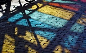 The shadow of a bicycle on a brick sidewalk.