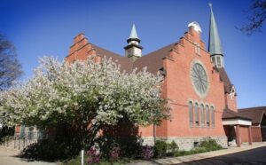 A brick church with a steeple and trees.