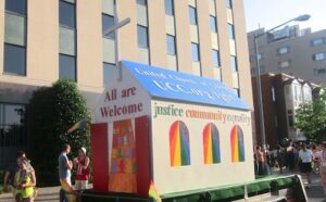 A float with a rainbow flag on it in front of a building.