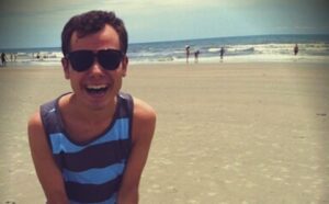 A man wearing sunglasses sitting on the beach.