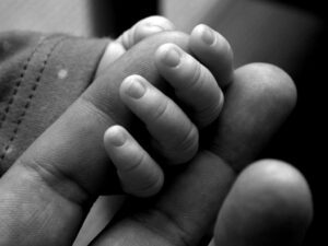 A black and white photo of a person holding a baby's hand.