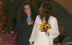 A woman with curly hair standing next to a woman with sunflowers.