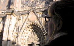 A woman wearing glasses is looking at an ornate cathedral.